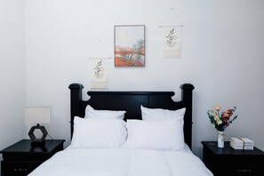 A neatly made bed with white linens, a black headboard, and a nightstand with a lamp and a vase of flowers. - Charming apartment in fabulous St. Mary Parish. 15 minutes away from Ocho Rios  (St. Mary Parish)