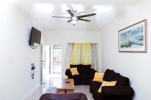 A living room with a ceiling fan, a flat-screen TV mounted on the wall, a sofa set, a coffee table, and a door leading outside. - Charming apartment in fabulous St. Mary Parish. 15 minutes away from Ocho Rios  (St. Mary Parish)