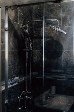 A glass-enclosed shower with a handheld showerhead and a wall-mounted faucet.