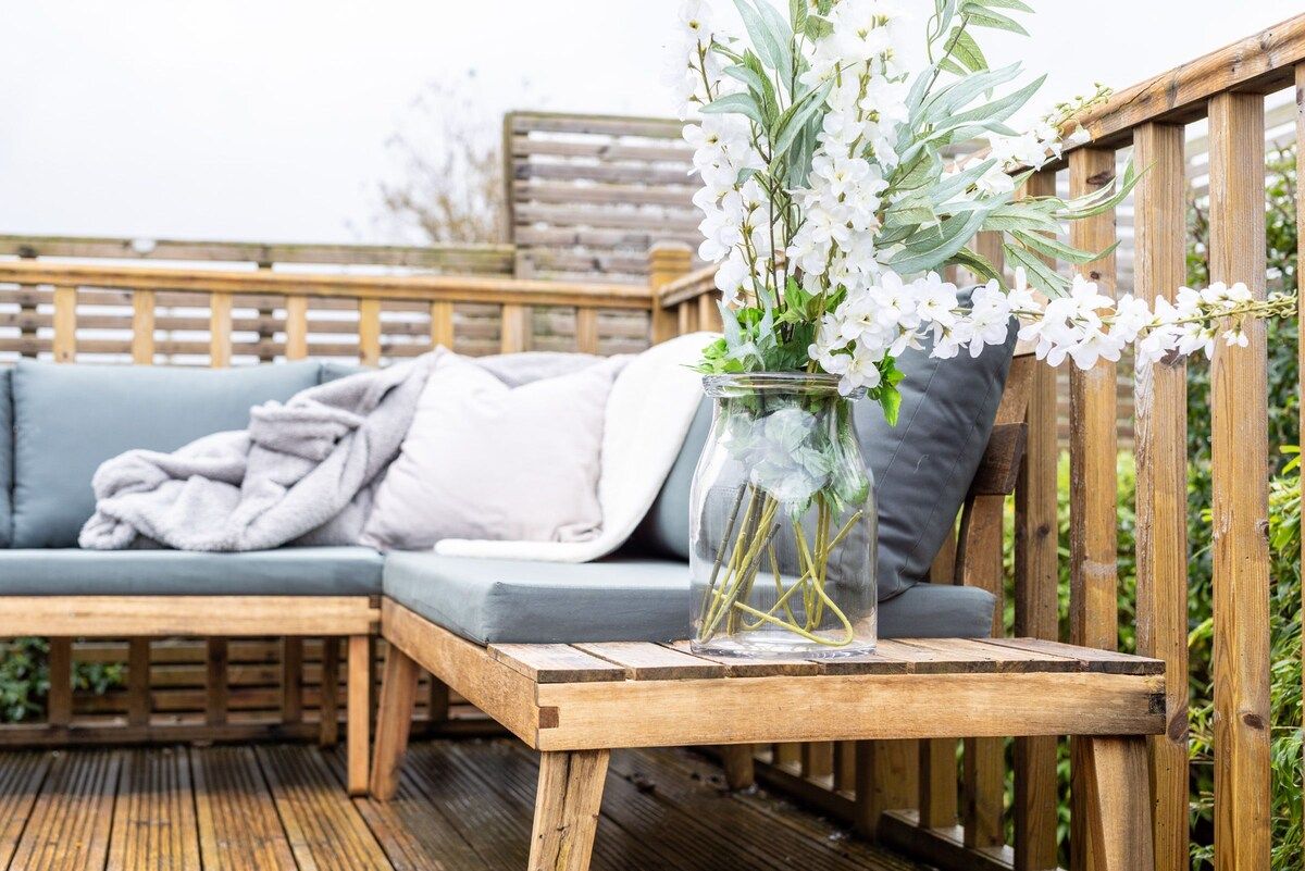 A wooden deck with a glass vase containing white flowers on a bench.