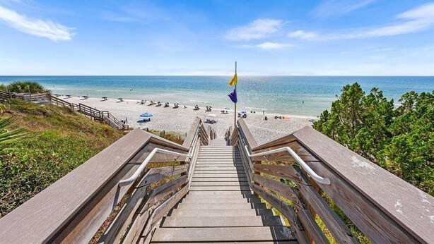 Una escalera de madera que lleva a una playa con una bandera en la parte superior.
