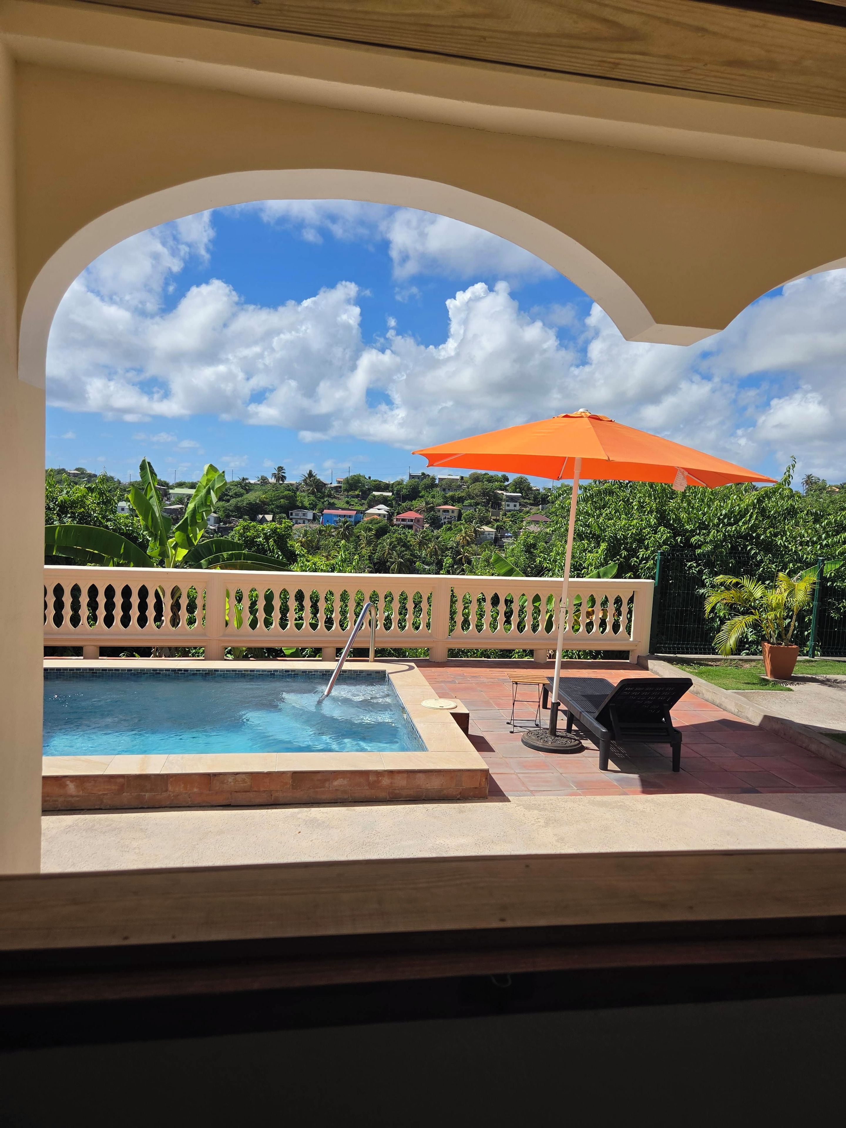 A pool area with a view of a residential neighborhood, a lounge chair, and an orange umbrella.