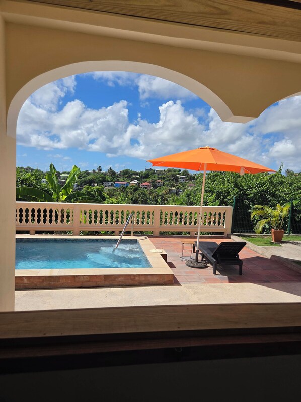A pool area with a view of a residential neighborhood, a lounge chair, and an orange umbrella.