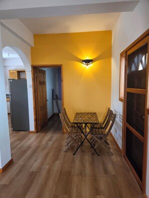 A dining area with a table and chairs, a wall-mounted light fixture, and a wooden door.