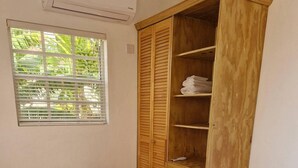 Een kamer met een houten garderobe, een raam met zonwering en een bed met kussens.