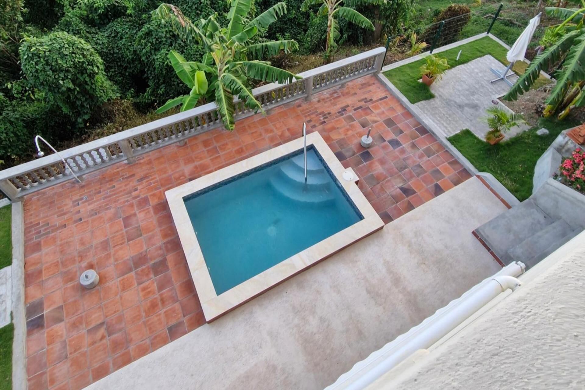 A rectangular swimming pool with a tiled deck, surrounded by a low brick wall and a metal railing.