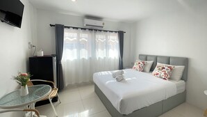 A hotel room with a bed, a TV, a desk with a chair, and a window with curtains. - Royal BJ Hotel (Pattaya)