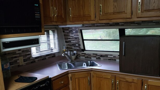 A compact kitchen with wooden cabinets, a built-in microwave, a sink, and a refrigerator. - Cozy primitive Rambler RV in Westport Renovo Pa river access  (Renovo)