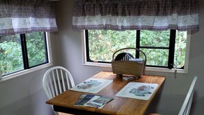 A dining area with a wooden table and white chairs, two windows with curtains, and a ceiling light fixture. - Cozy primitive Rambler RV in Westport Renovo Pa river access  (Renovo)