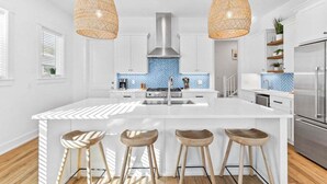 A modern kitchen with a central island, white cabinetry, a blue herringbone backsplash, and two hanging wicker pendant lights.