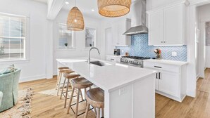 A modern kitchen with a large island, white cabinetry, and a blue herringbone backsplash.