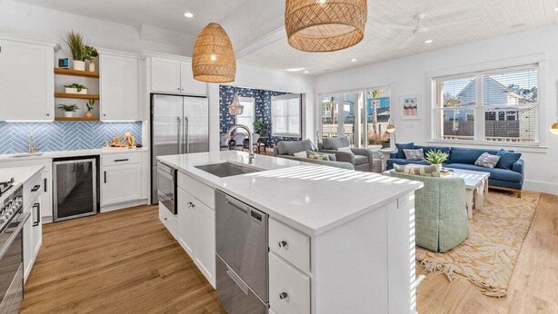 A modern kitchen with white cabinetry, a central island, and a dining area with a blue sofa and a coffee table.