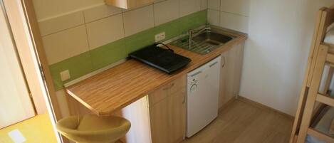 Una cocina compacta con microondas, lavabo y un taburete pequeño.