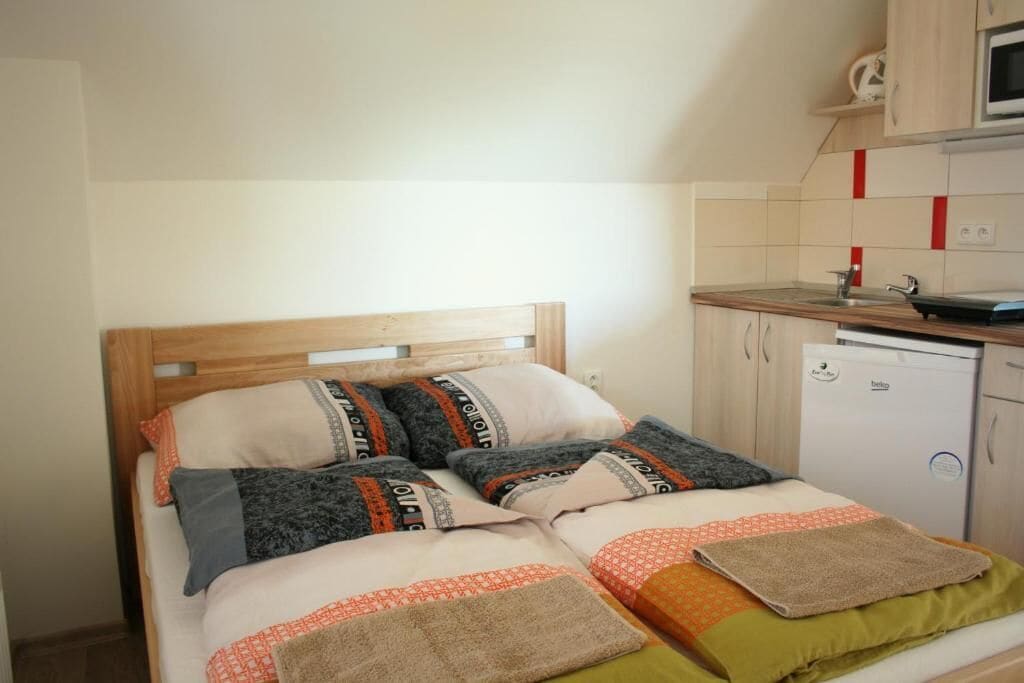 A bedroom with a wooden headboard, a bed with patterned bedding, and a kitchenette with a microwave and a small refrigerator.