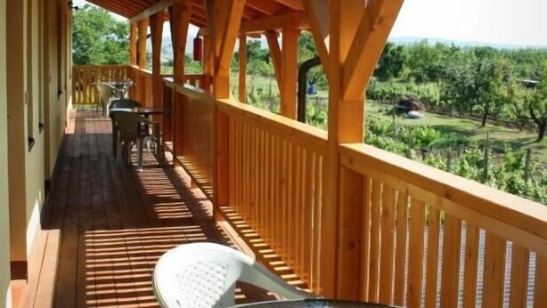 A wooden deck with a glass table and chairs, overlooking a lush landscape.
