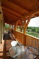 Terraza de madera con mesa y sillas de vidrio, con vistas a un paisaje exuberante.