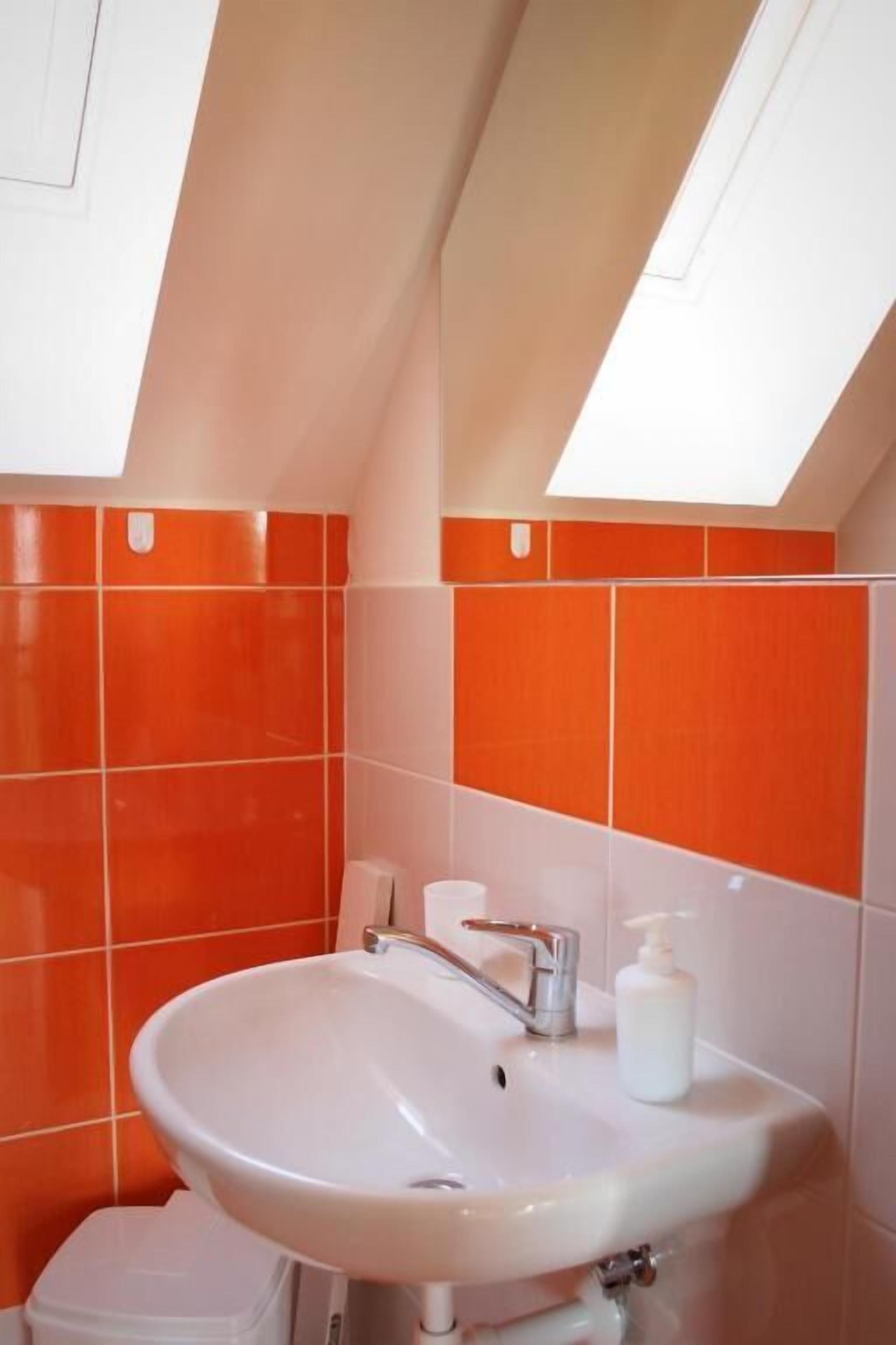 A bathroom with a white sink, orange tiles, and a skylight.