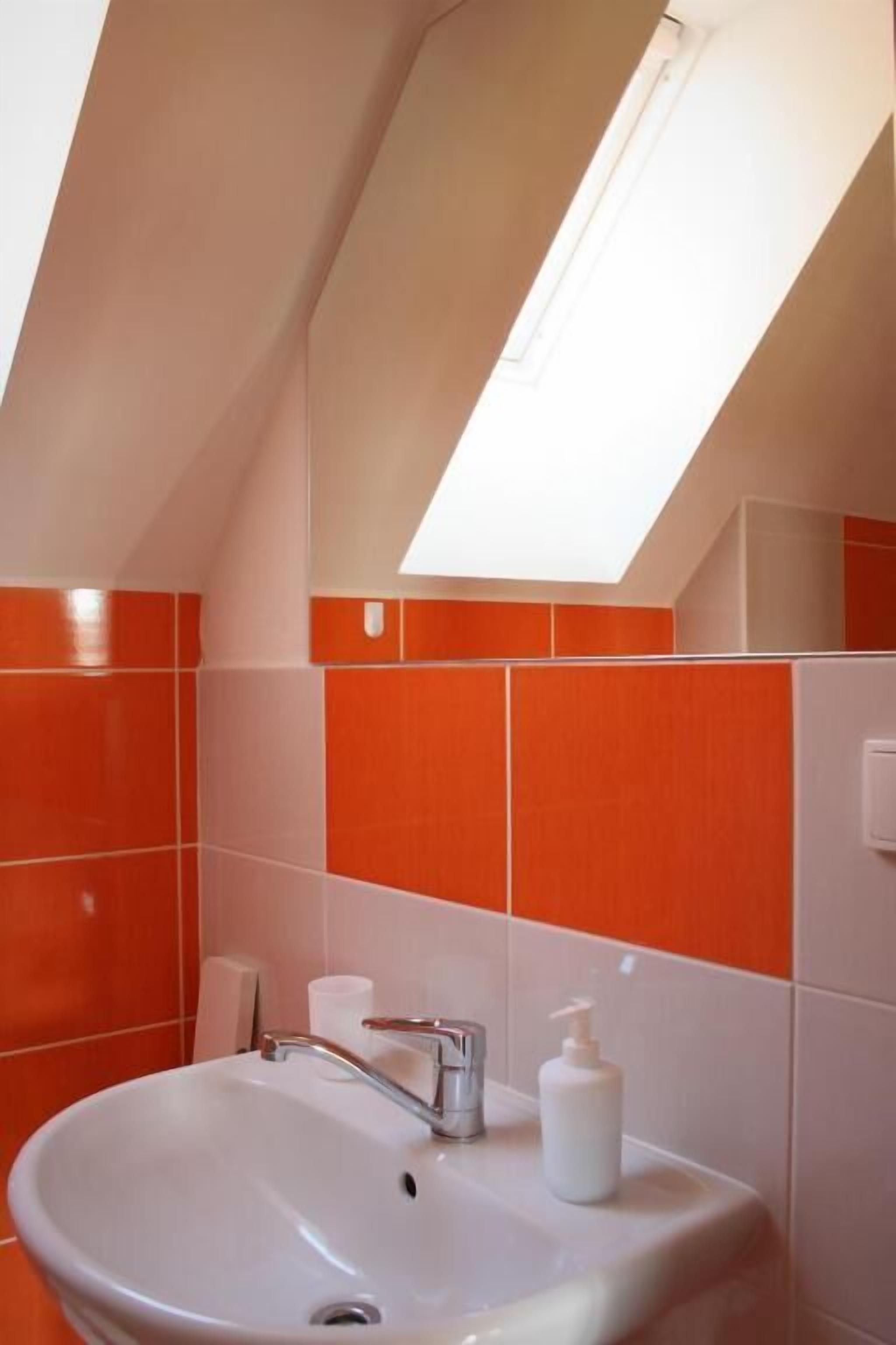 A bathroom with a skylight, orange and white tiles, a sink, and a mirror.
