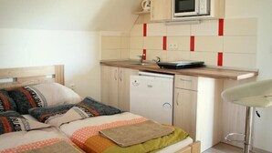 A compact bedroom with a bed, bedside table, and a small kitchenette with a microwave and a dishwasher.