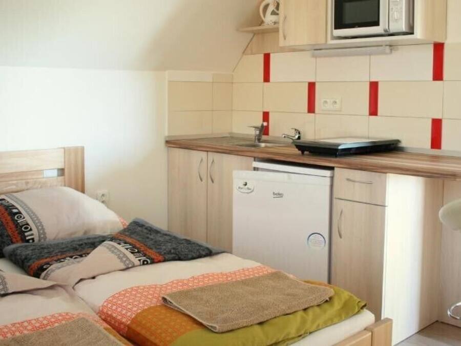 A compact bedroom with a bed, bedside table, and a small kitchenette with a microwave and a dishwasher.