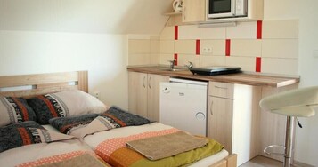 Un dormitorio compacto con cama, mesita de noche y una pequeña kitchenette equipada con microondas y lavavajillas.