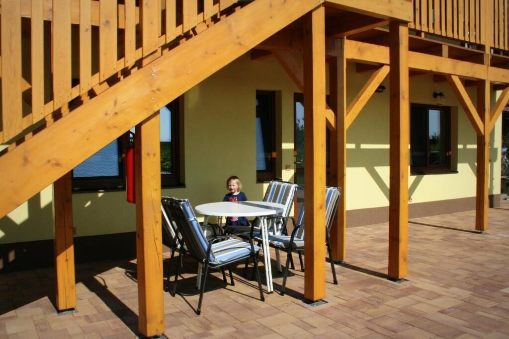 An outdoor patio with a wooden pergola, a round table, and striped chairs.