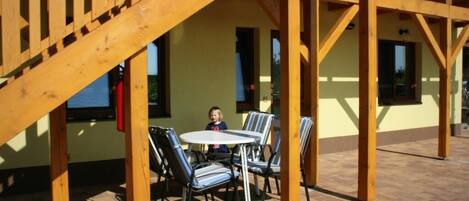 An outdoor patio with a wooden pergola, a round table, and striped chairs.
