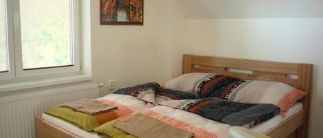 A bedroom with a wooden bed, a window with blinds, a radiator, and a painting on the wall.