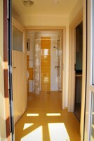 Un pasillo con zona de ducha, una puerta que da a una habitación y suelo de baldosas.