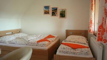 A bedroom with two wooden beds, a chair, and three framed pictures on the wall.