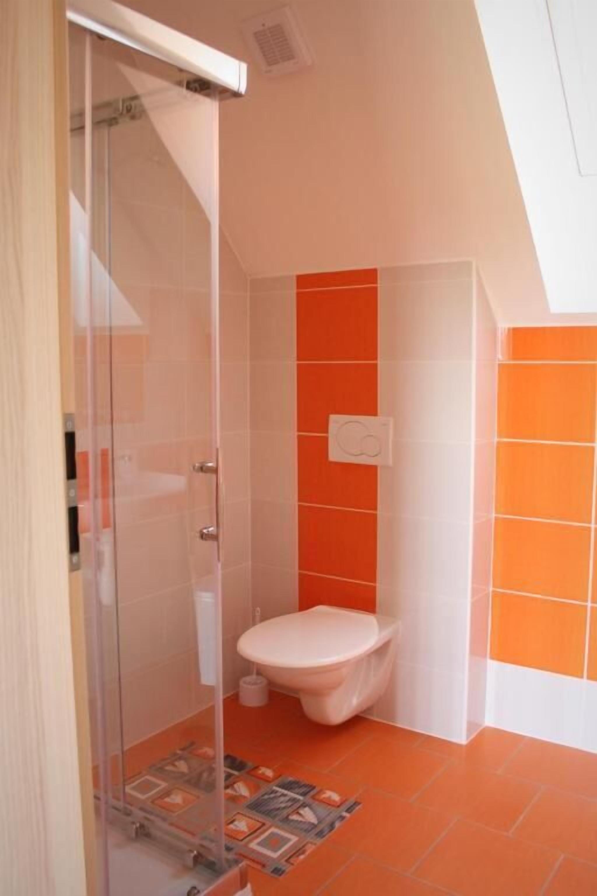A bathroom with a glass shower enclosure, a white toilet, and orange and white tiled walls.