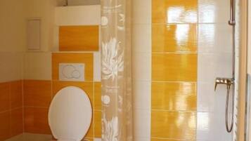 Un baño con inodoro, ducha y pared de azulejos en una combinación de amarillo y blanco.