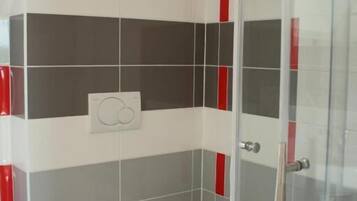 A small bathroom with a toilet, a shower, and a glass door.
