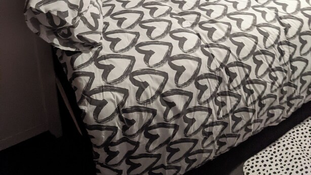 Ein Bett mit einem gemusterten Überwurf, einem Kopfkissen und einer Wand mit dekorativer Tapete.