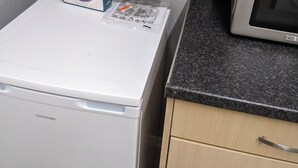 Eine kleine Küche mit einem weißen Kühlschrank, einer Mikrowelle auf einer Granit Arbeitsplatte und einem Karton mit der Aufschrift 'RICE SNAPS' auf dem Kühlschrank.