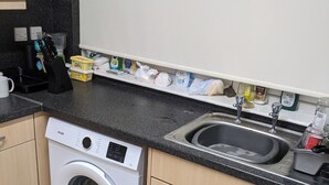 Eine kleine Küche mit einer Waschmaschine, einem Spülbecken und verschiedenen Küchenutensilien auf der Arbeitsfläche.