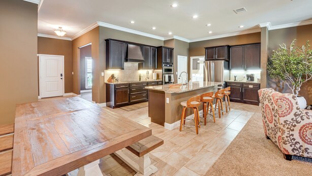 A spacious kitchen with dark cabinets, a large island with bar stools, and a dining area with a wooden table. - 11 Mi to Dtwn: Lubbock Home w/ Patio, Grill & Yard (Lubbock)