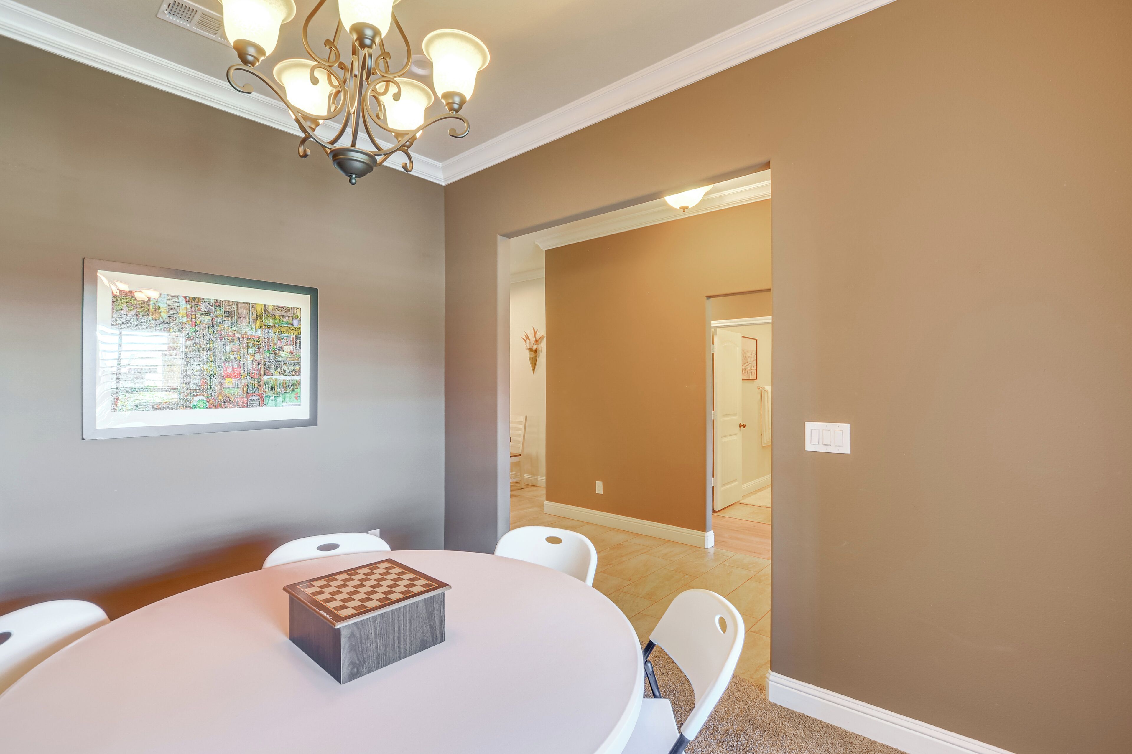 Un coin repas avec une table ronde, des chaises, un lustre et une œuvre d’art encadrée au mur.