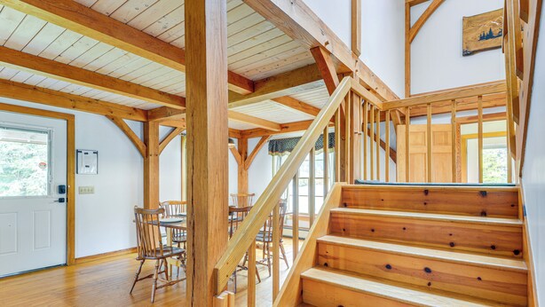Una escalera de madera que conduce a un nivel superior, un comedor con sillas y una mesa de madera, y una puerta con ventana.