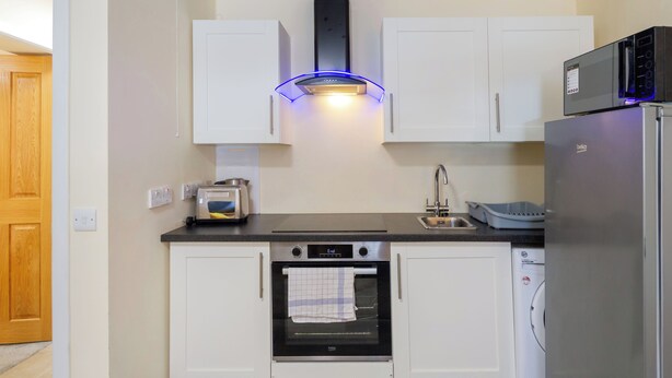 A compact kitchen with white cabinets, a built-in oven, a microwave, and a toaster. - Central 2-Bed Flat near Edinburgh’s Highlights (Edinburgh)