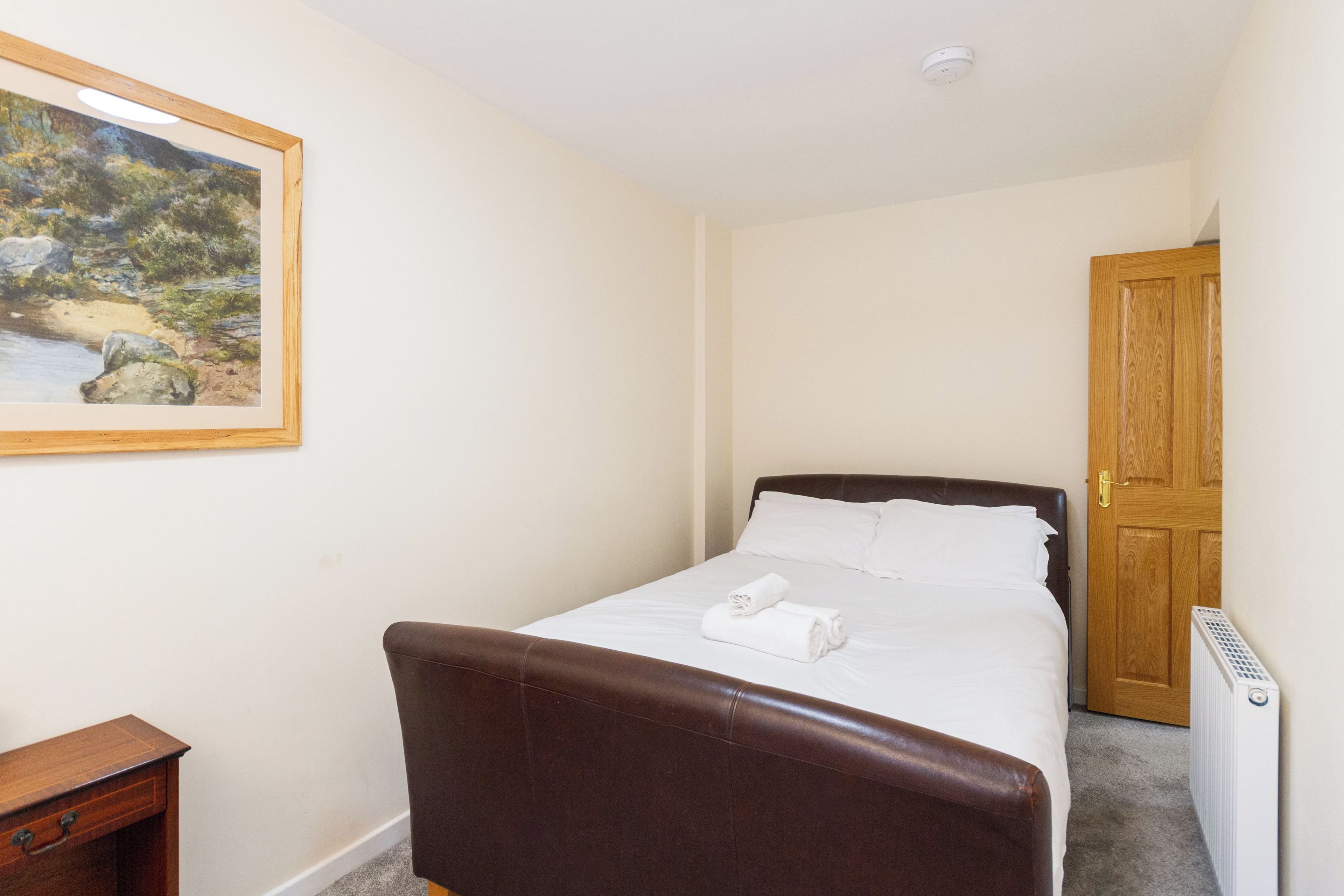 A hotel room with a bed, a bedside table, a chair, a painting on the wall, and a door.