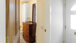 A hallway with a wooden door, a white wall, and a brown dresser with drawers. - Central 2-Bed Flat near Edinburgh’s Highlights (Edinburgh)