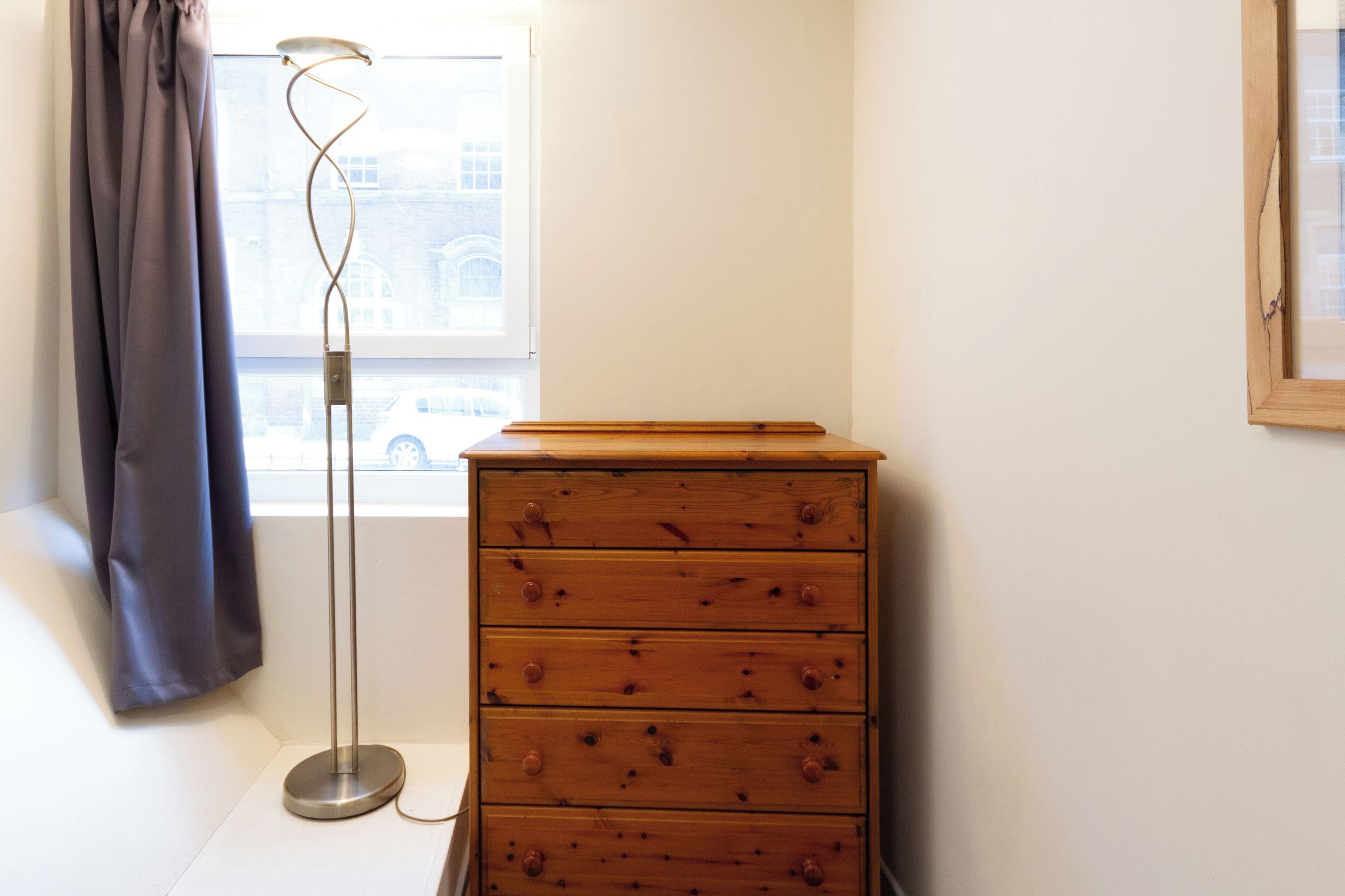 A room with a wooden dresser, a floor lamp, and a window with curtains.