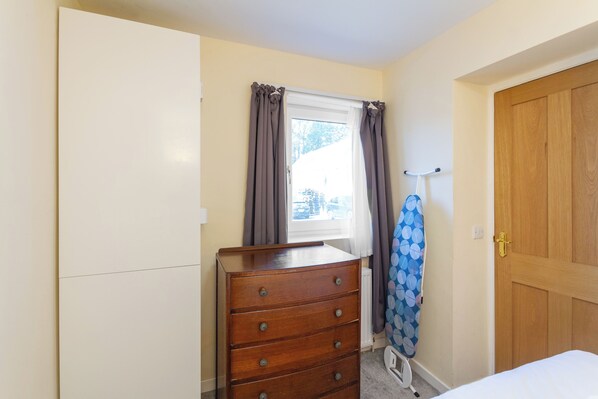 A bedroom with a wooden dresser, a window with curtains, a door, and a bed.