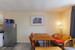 A compact living space with a kitchenette, a dining table with chairs, and a single bed.