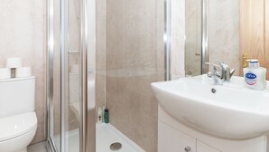 Un baño moderno con ducha de vidrio, lavamanos blanco y un inodoro.