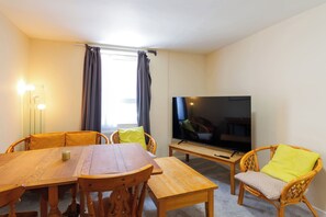 A living room with a wooden table, wicker chairs, a flat-screen TV, and a window with curtains. - Central 2-Bed Flat near Edinburgh’s Highlights (Edinburgh)