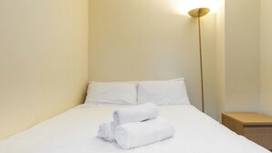 A neatly made bed with white linens and two rolled towels, a bedside table, and a floor lamp. - Central 2-Bed Flat near Edinburgh’s Highlights (Edinburgh)