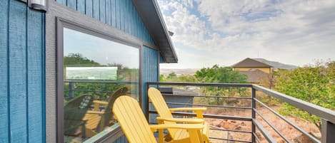A balcony with Adirondack chairs, a glass door, and a view of a mountainous landscape.