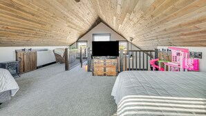 Un dormitorio con techo inclinado, cama, cómoda, escritorio y una casita de juegos rosa.